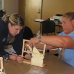 Two workshop participants use a model made of nuts, bolts, and popsicle sticks to simulate buildings in an earthquake. They practice different methods to make the building robust against shaking.